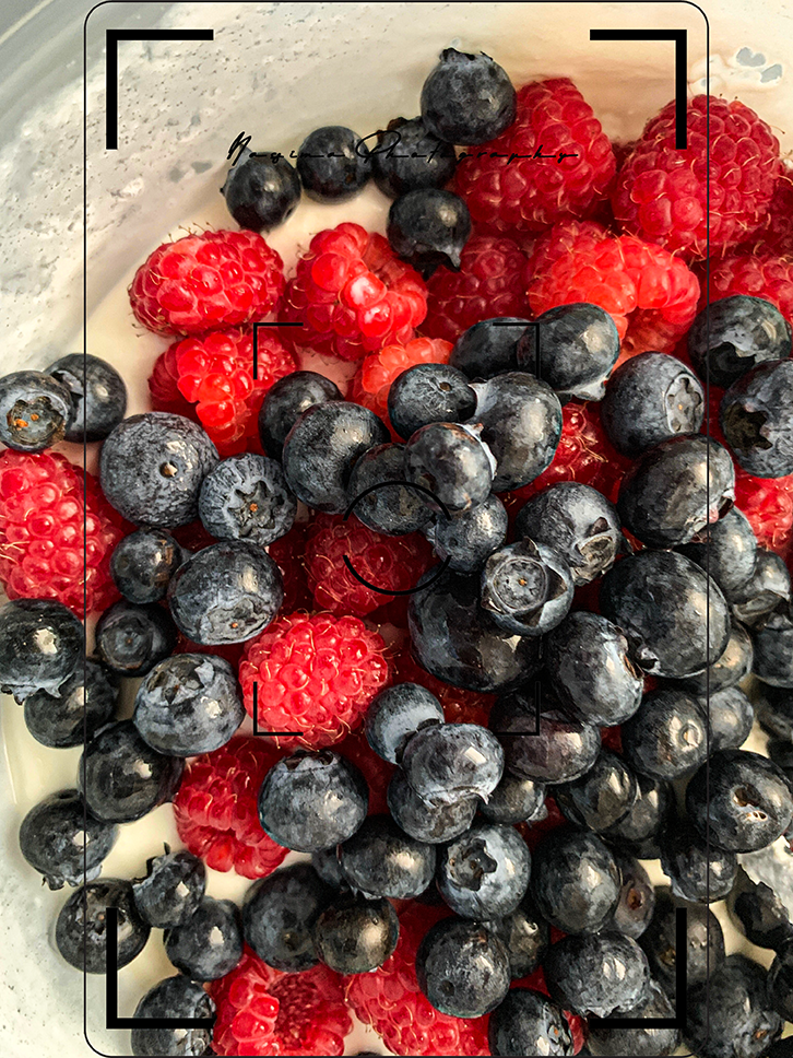 Nahaufnahme von frischen Himbeeren und Heidelbeeren auf Joghurt.