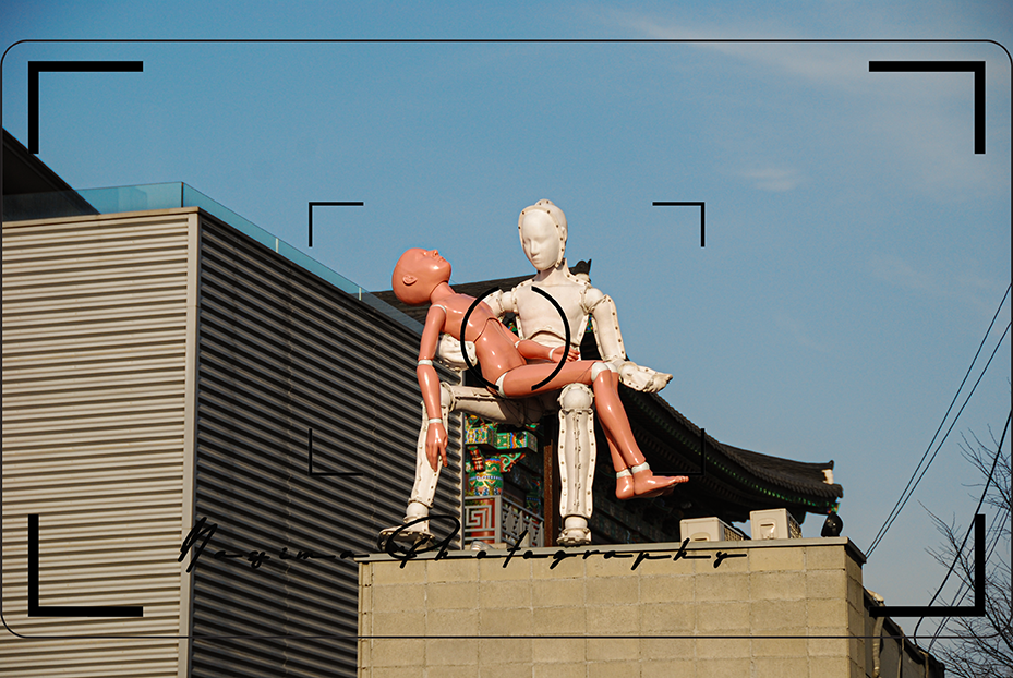 **Alt-Text:**
`Kunstinstallation mit zwei Crash-Test-Dummys auf einem Gebäudedach in Seoul, Südkorea.`
