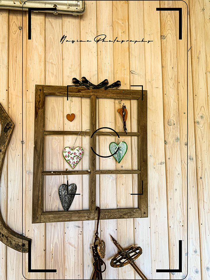 Altes Holzfenster mit dekorativen Herzen und kleinen Vogelfiguren an einer hellen Holzwand.